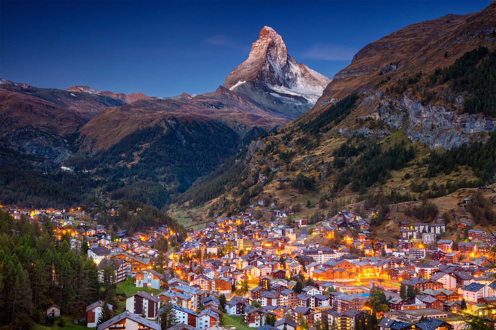 Mountain village in Switzerland illuminated at twilight. Contact Prism for visa support.